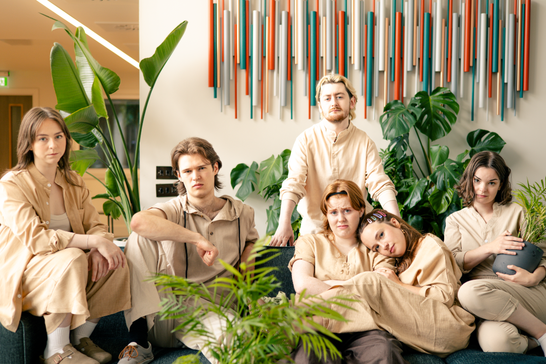 6 people wearing beige clothes sit together and look at the camera.