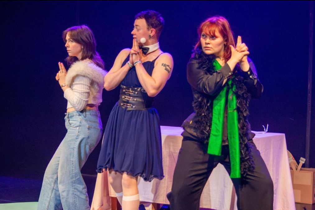 3 people stand on a stage making handguns and looking out.